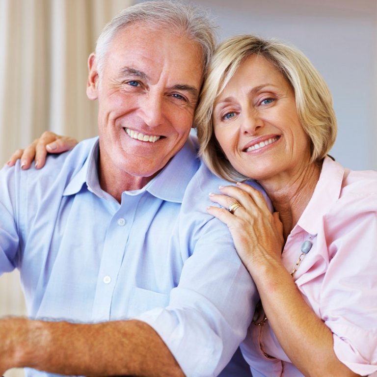 an elderly couple looking into a camera and showing off their smile